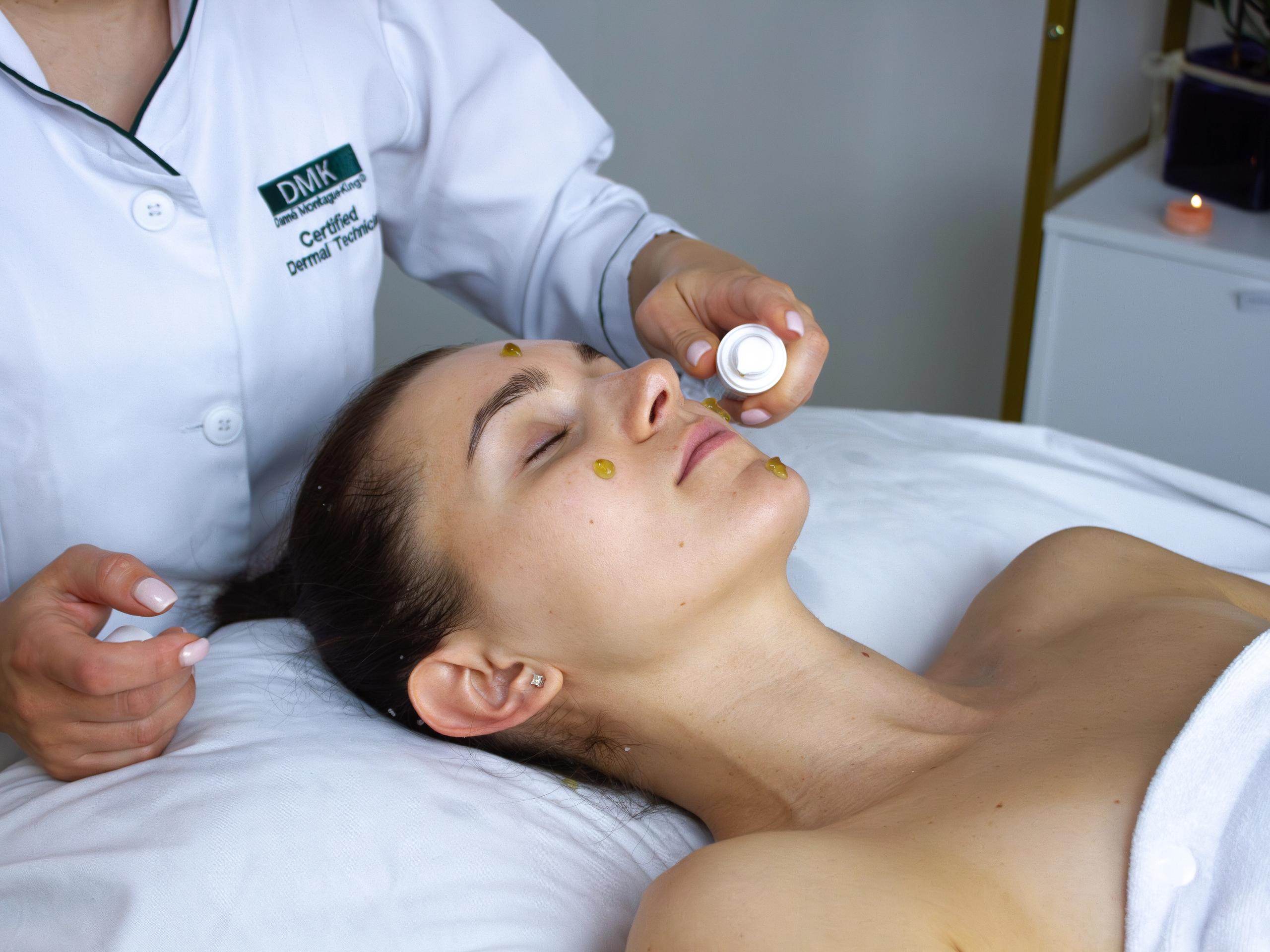 A technician is applying yellowish product to a woman's face