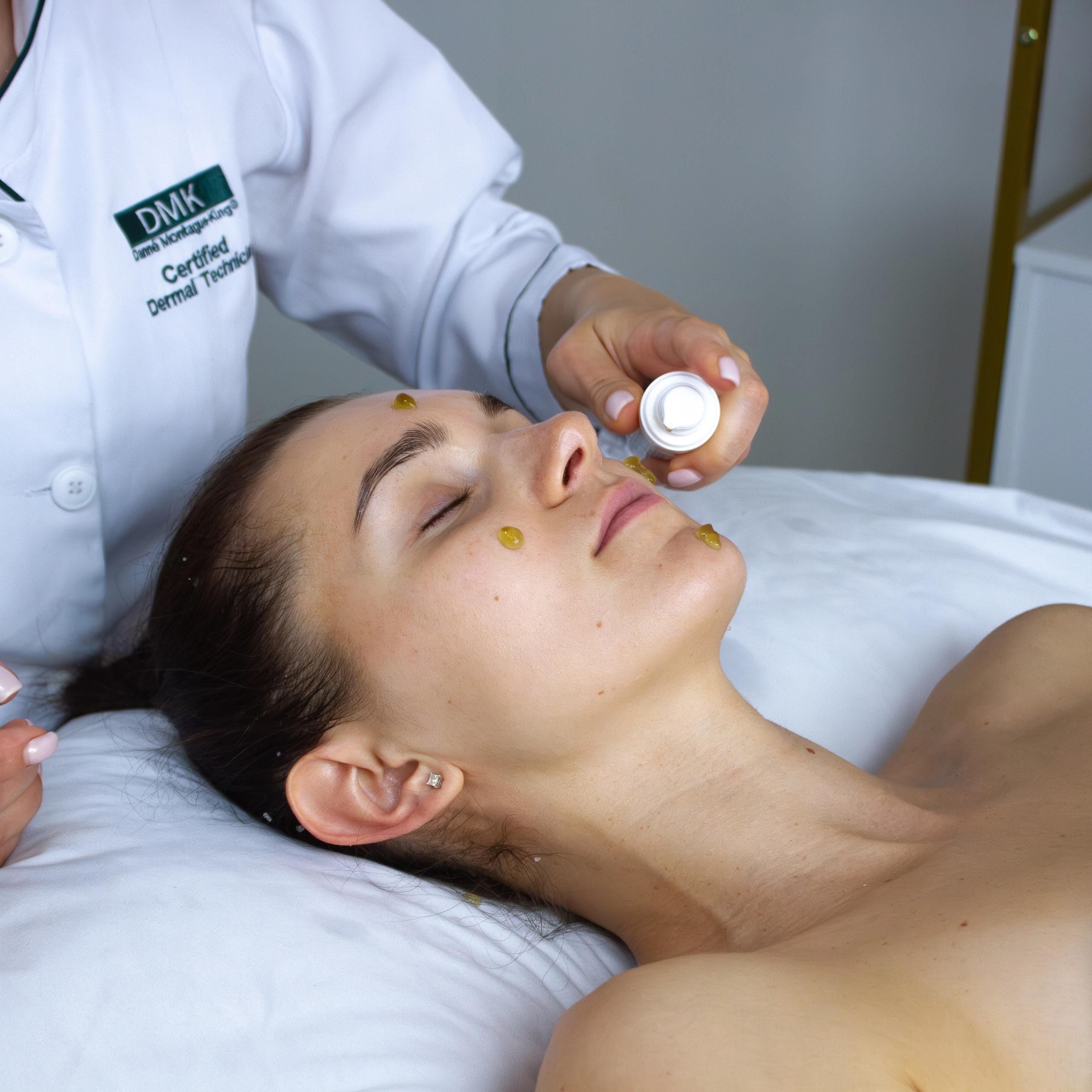 A technician is applying yellowish product to a woman's face