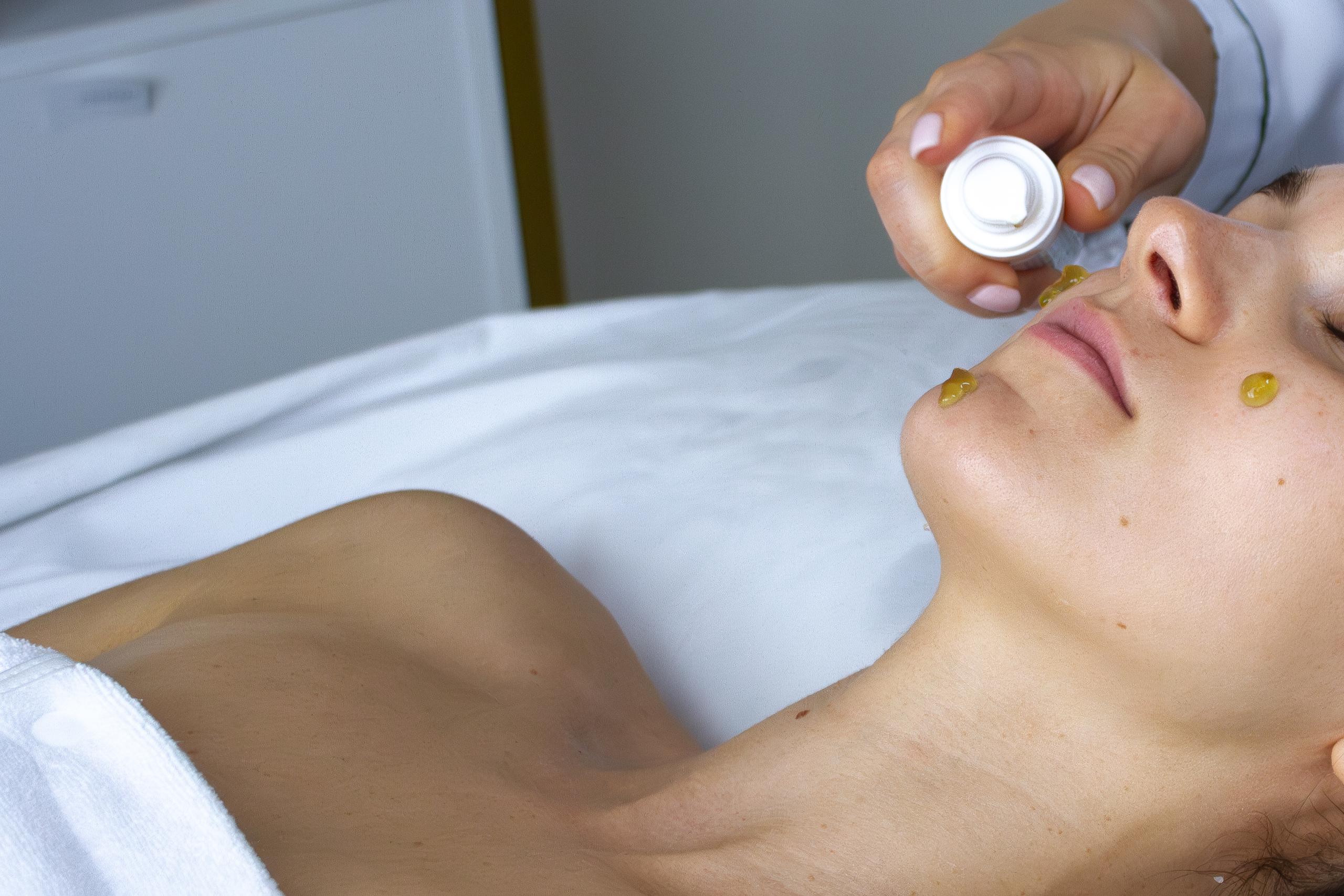 Close-up of a yellowish skincare product being applied to a woman't face