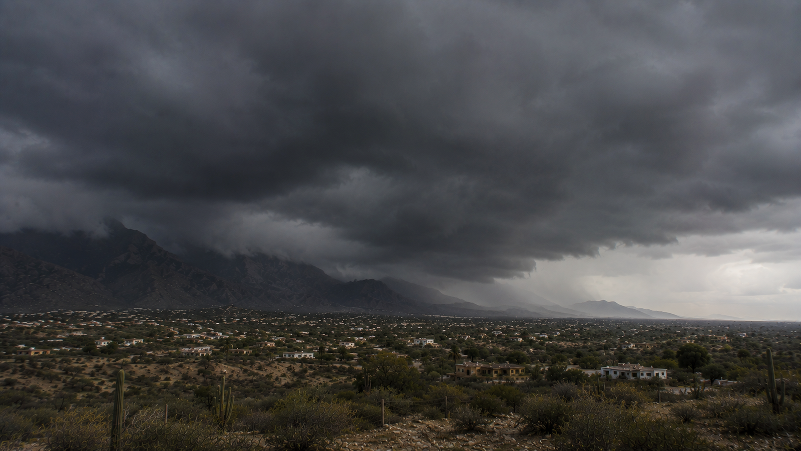 Dark tropical storm clouds over a Baja California Sur desert community and mountain range.