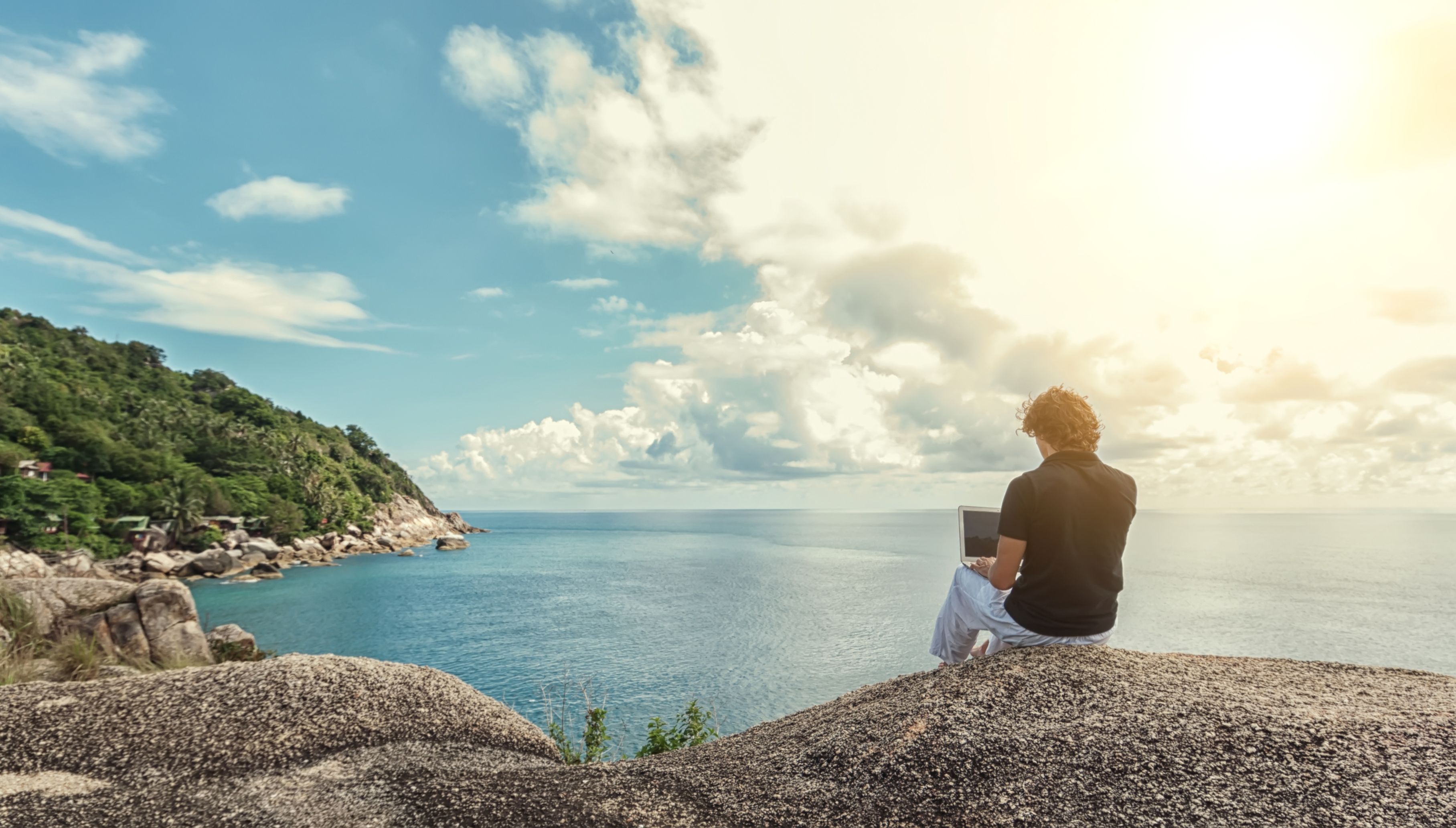A man working on a laptop remotely in front of the sea