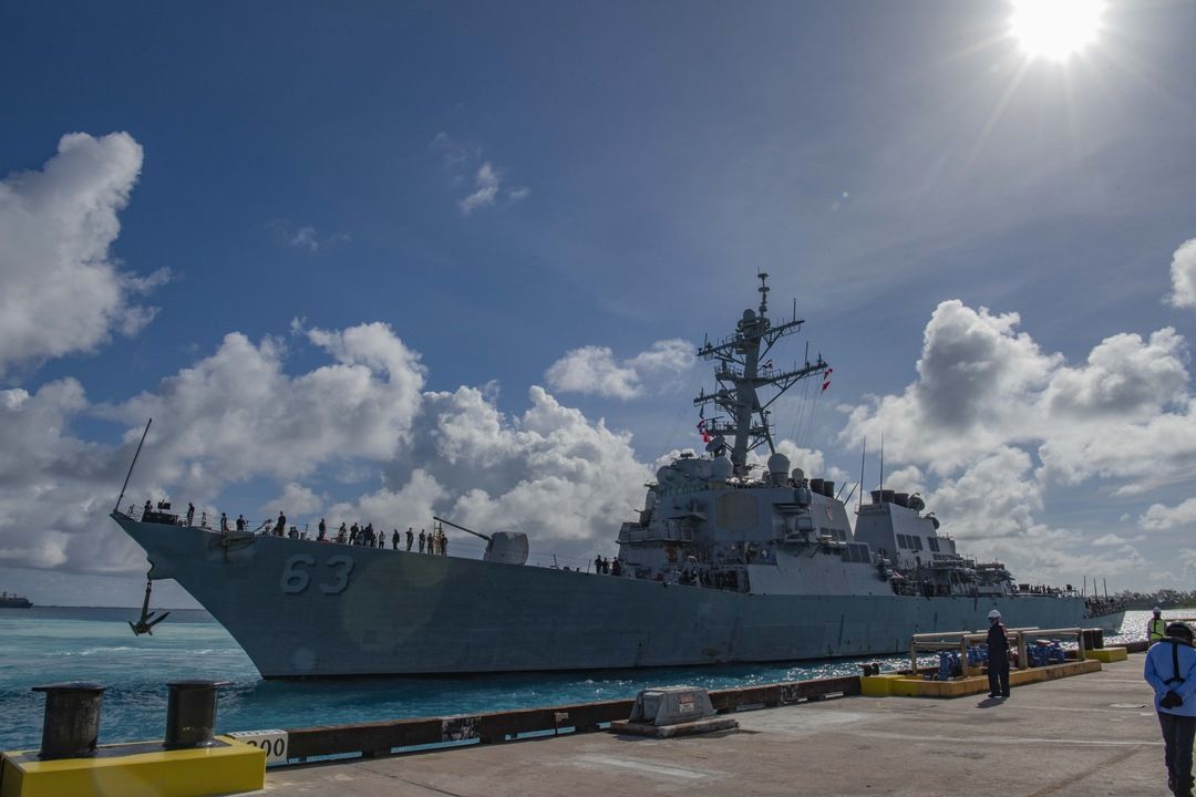 US Navy destroyer 63 arriving pierside with sailors on deck under tropical clouds