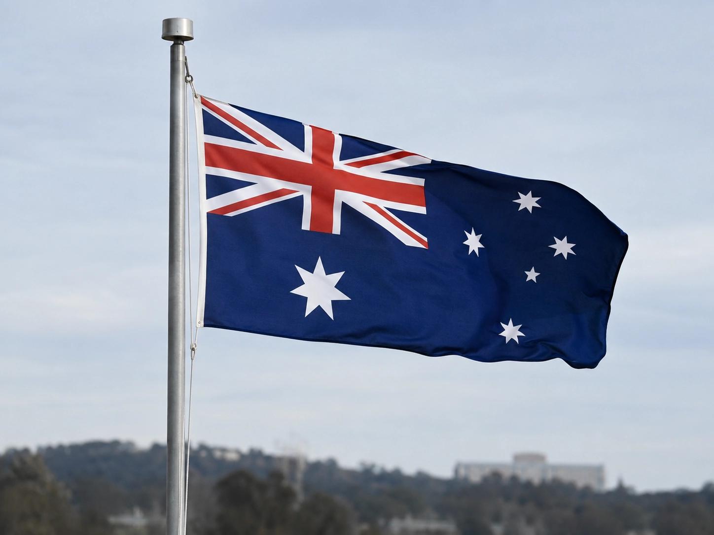 Australian flag rippling on a flagpole above Canberra with Parliament House visible in the distance