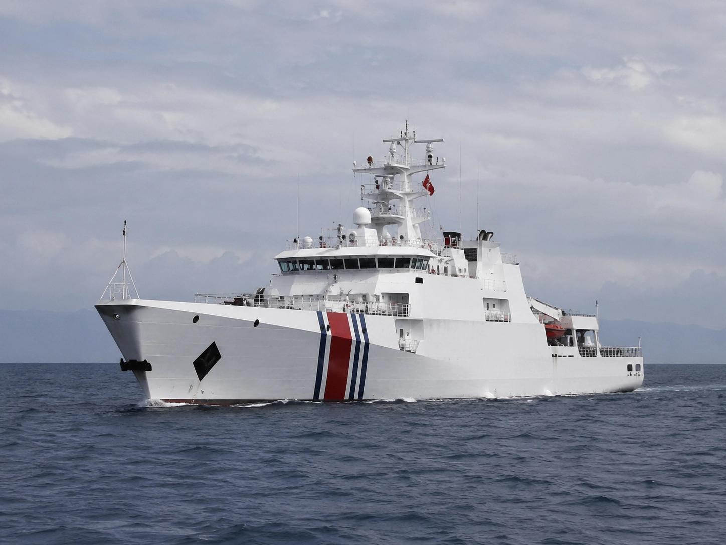 White coast guard patrol ship with red and blue stripes cutting through open water