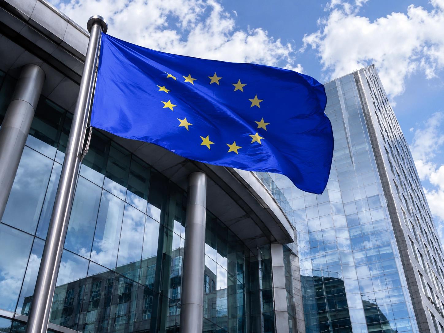 European Union flag flying in front of glass EU headquarters buildings
