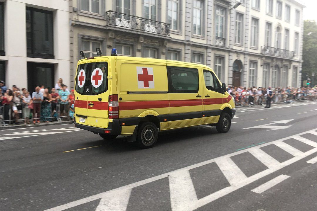 Yellow ambulance with red crosses driving along a city street past crowds