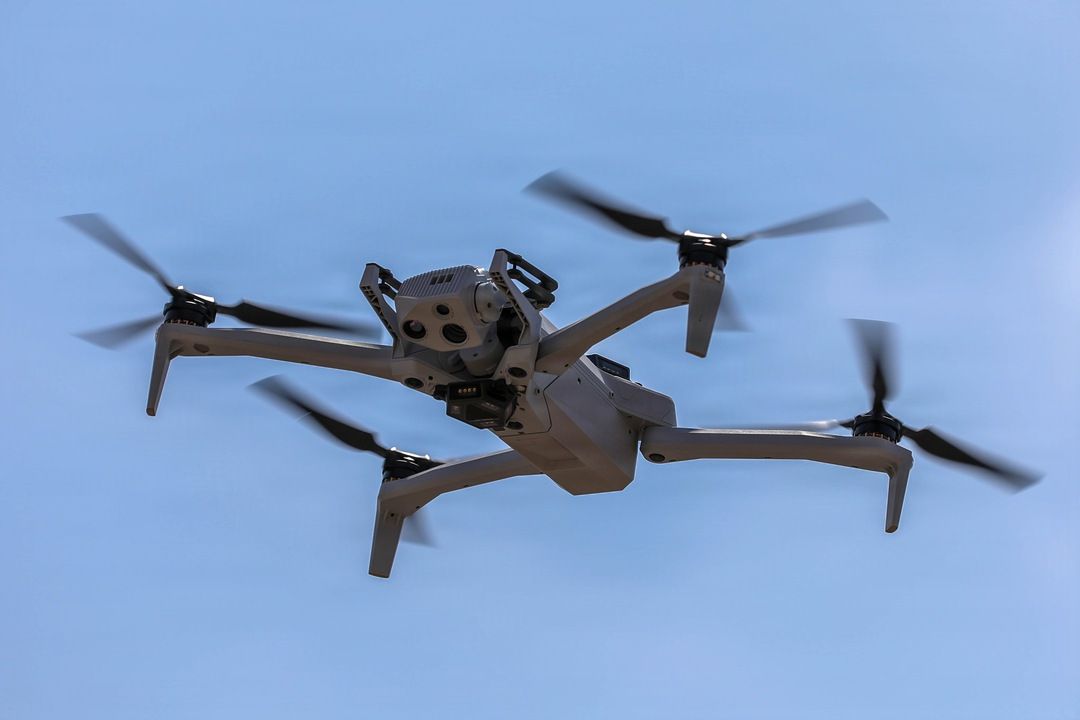 Military quadcopter drone in flight against a pale blue sky
