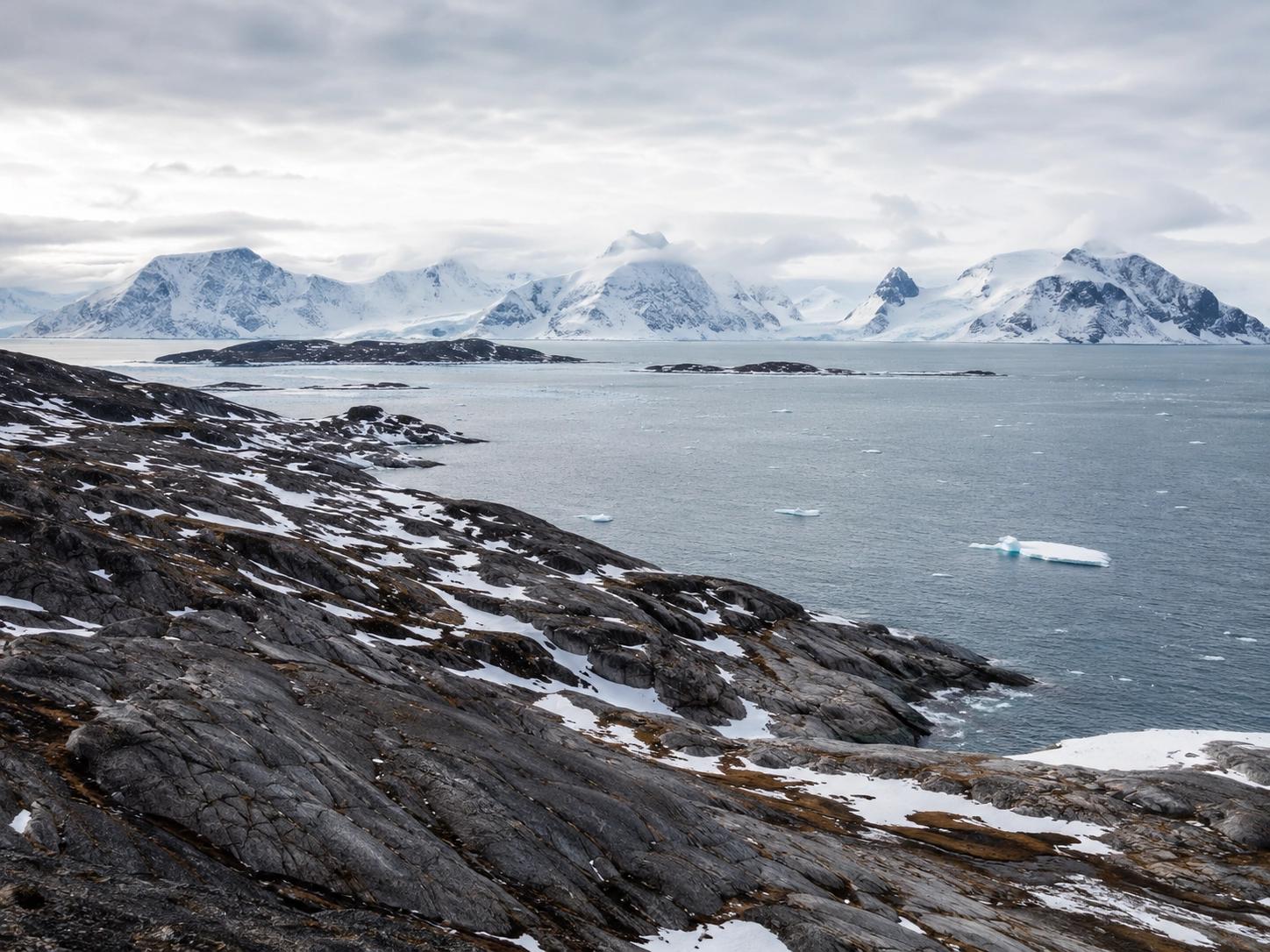 Rocky Arctic coastline overlooking a bay dotted with icebergs and snow-capped mountains