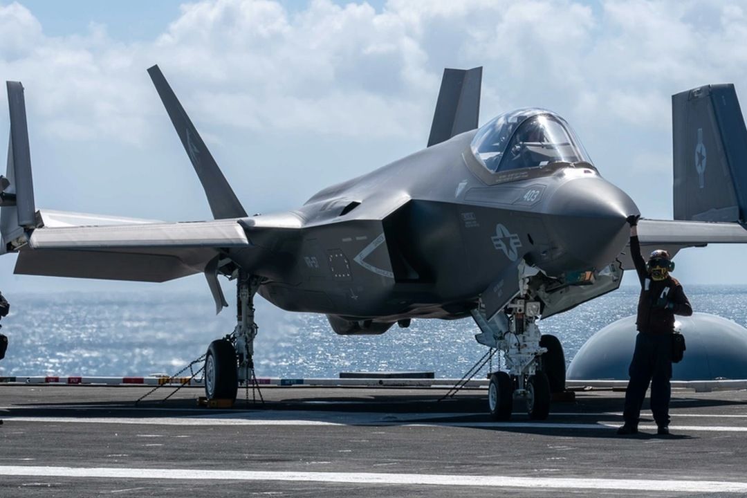 F-35C stealth fighter parked on an aircraft carrier flight deck with crew member