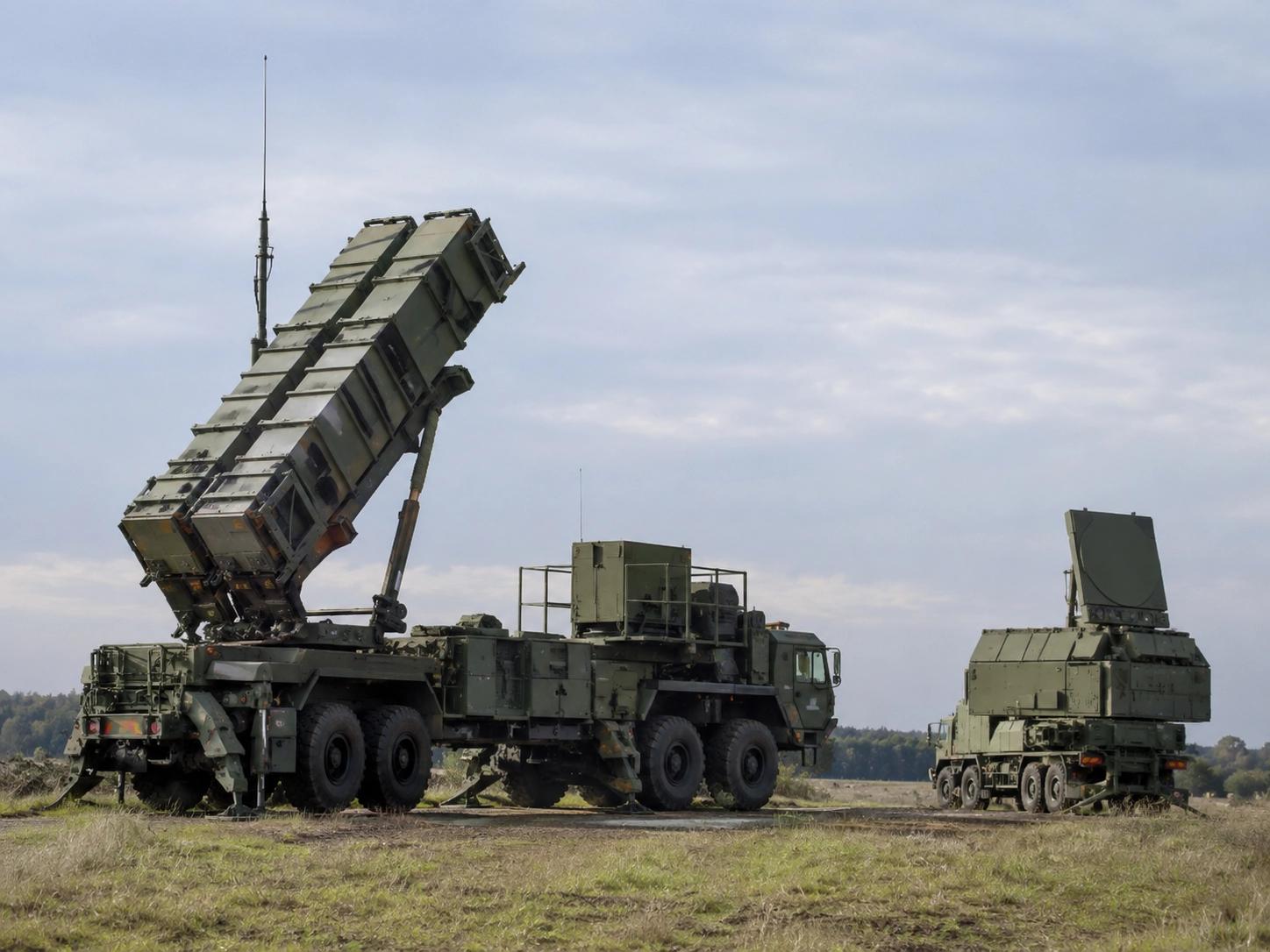 Patriot missile launcher with raised canisters beside a radar unit in an open field