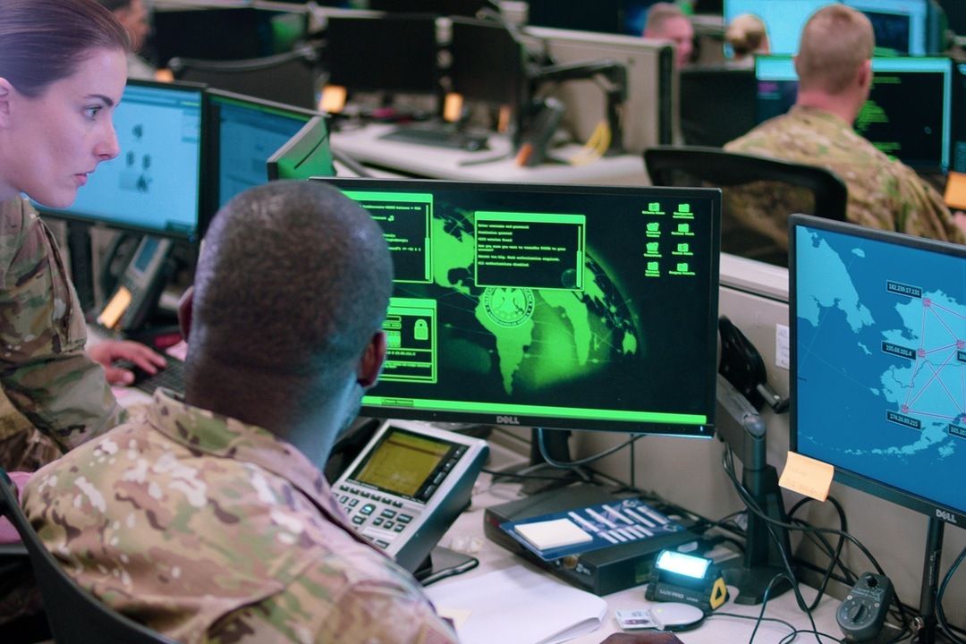 Soldiers in camouflage working at monitors showing green cyber maps
