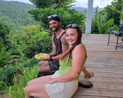 Two smiling guests relax on a wooden deck with scenic rainforest views in the background, enjoying tropical fruit after a La Vista Rides experience in El Yunque, Puerto Rico.