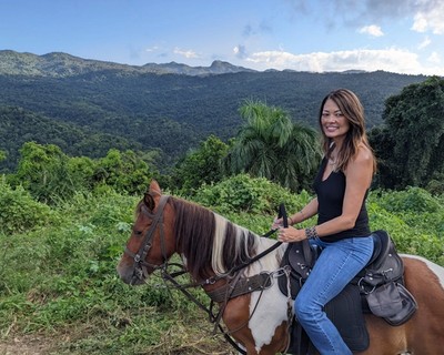 A smiling guest rides a paint horse along a scenic ridge with sweeping views of lush green mountains and rainforest canopy during a Lavista Rides tour in El Yunque, Puerto Rico.