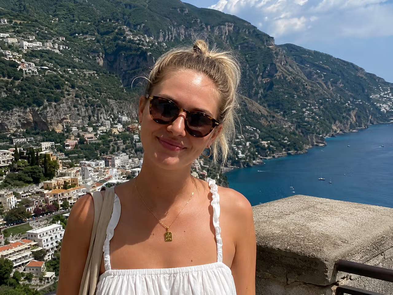 Mulher sorrindo gravando na costa italiana, cenário ideal para música de fundo para vlog.