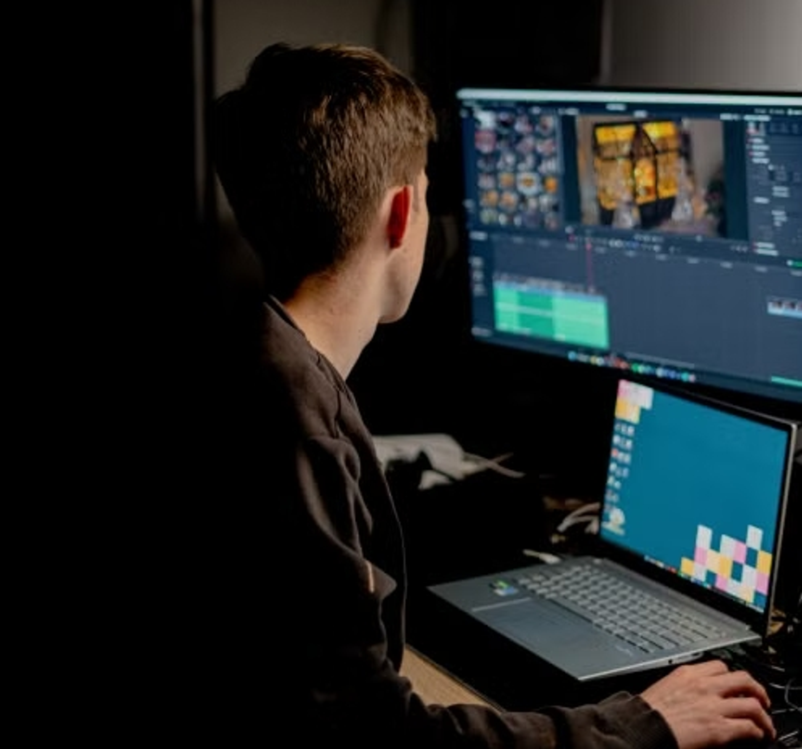 A video editor working on dual monitors in a dark room, selecting the perfect music for travel videos.