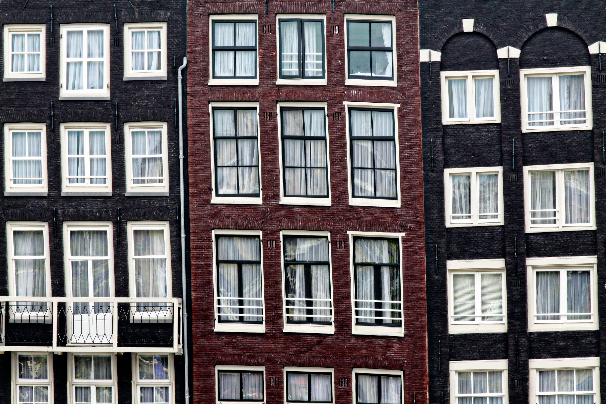 Fachadas estreitas de tijolo na Warmoesstraat, em Amsterdã, visivelmente fora de prumo e inclinadas umas em direção às outras.