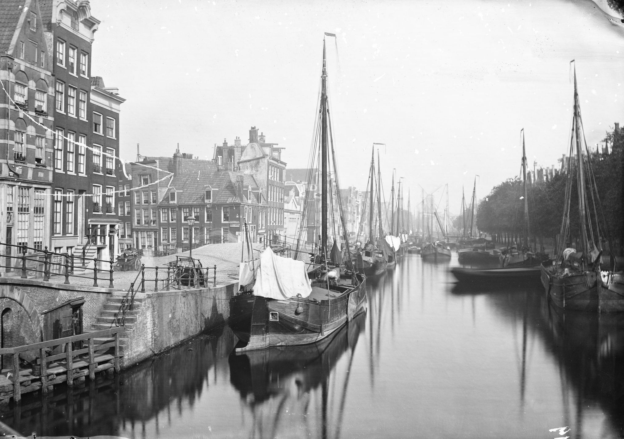 Fotografia de cerca de 1870: a Brouwersgracht, números 101 a 119, vista em direção ao oeste, com barcos de carga de mastros atracados ao longo do cais e fachadas de armazéns; à esquerda, a entrada da Lindengracht.