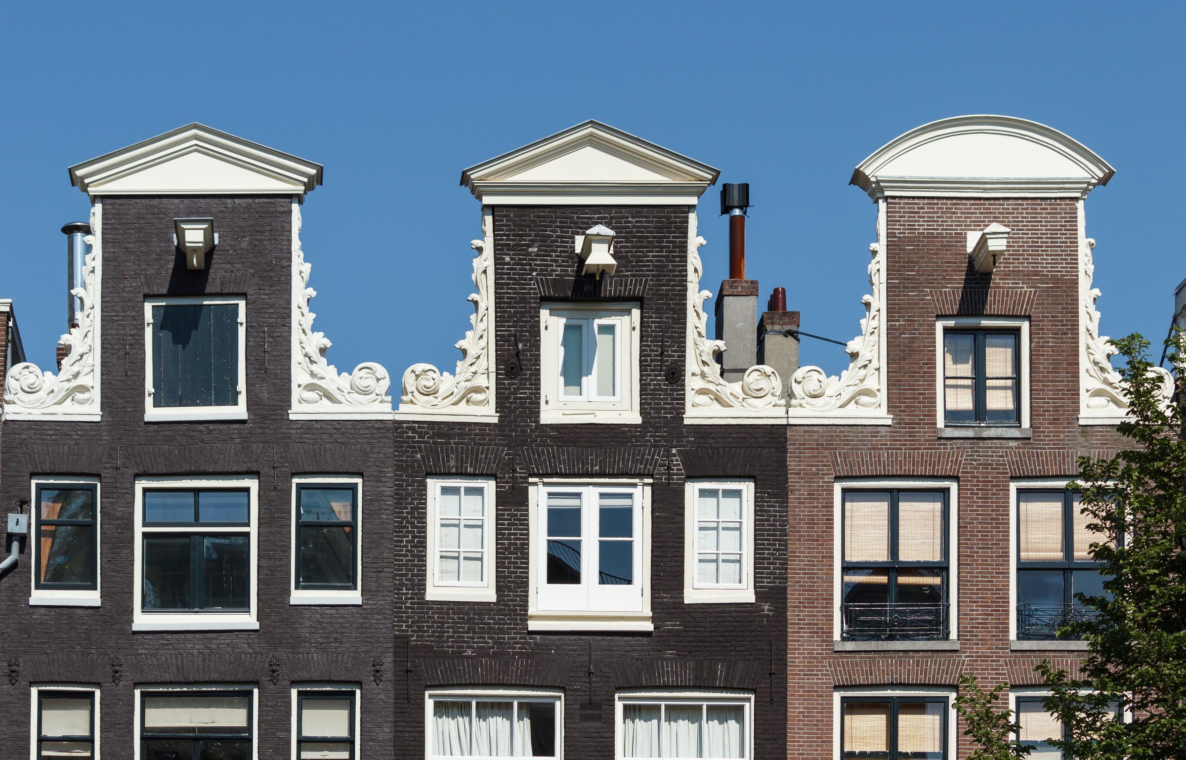 Topos de três fachadas de tijolo com frontões de pescoço na Prinsengracht, números 1037 a 1041, cada um com uma viga de içamento projetada no alto.