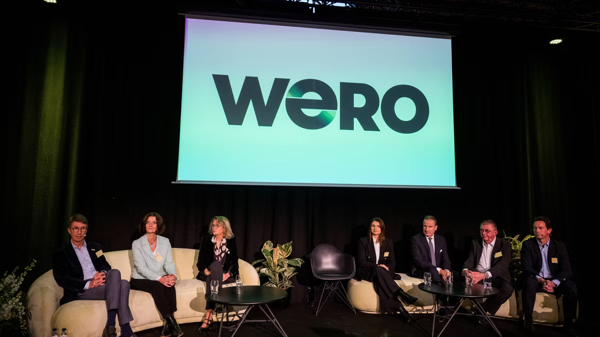 Seven panellists seated on stage in front of a large screen showing the Wero logo.