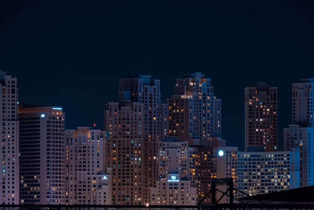 A cluster of lit residential tower blocks at night against a dark blue sky.