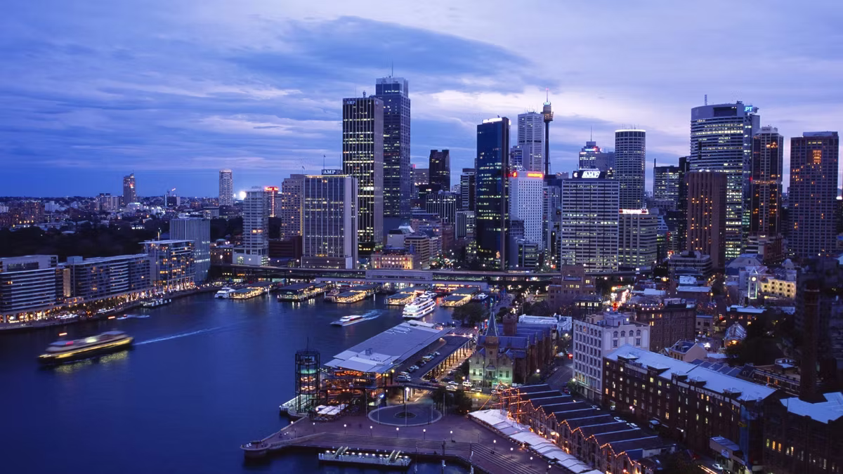 Sydney at dusk from above, ferries at Circular Quay in the foreground and the central business district towers lit behind.
