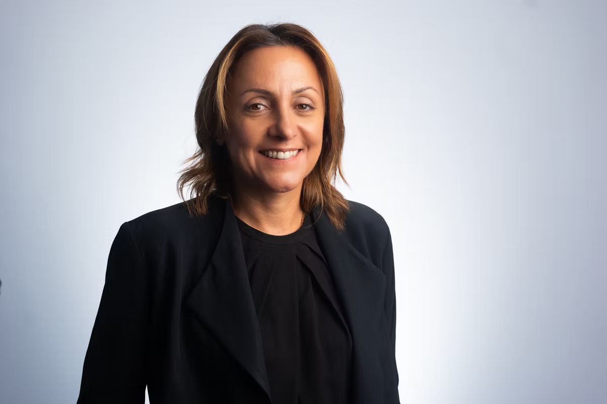 VISA Regional Senior Vice President Leila Serhan in a black blazer stands against a light gray background, conveying a professional and friendly demeanor.