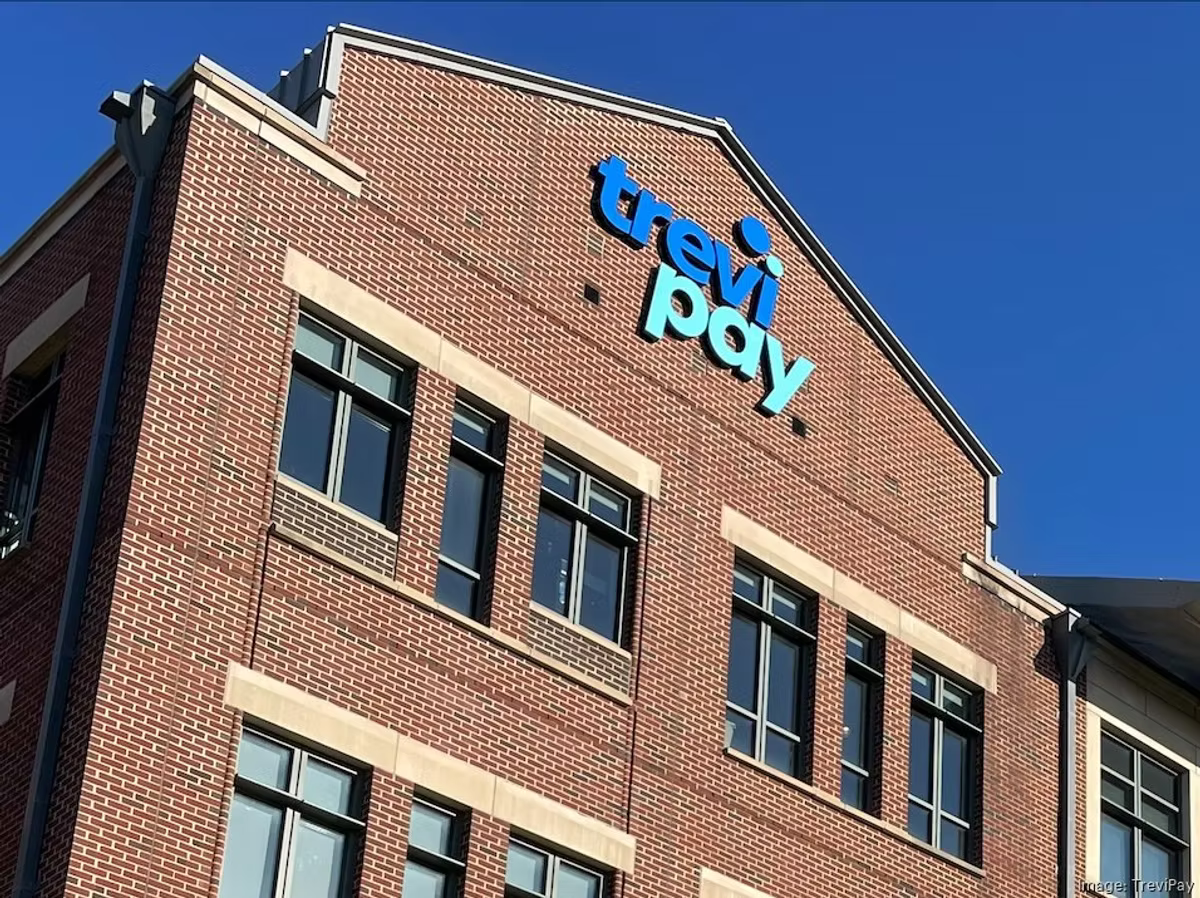 The TreviPay logo mounted on the brick facade of an office building against a clear blue sky.