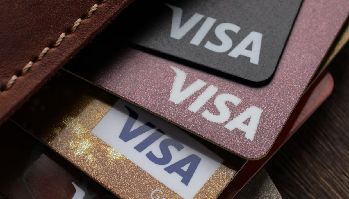 Close-up of several Visa cards in black, pink and gold fanned out of a brown leather wallet.