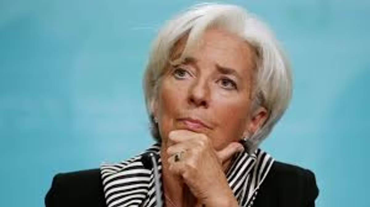 A woman with short white hair in a black jacket and striped collar rests her chin on her hand, photographed against a pale blue backdrop.