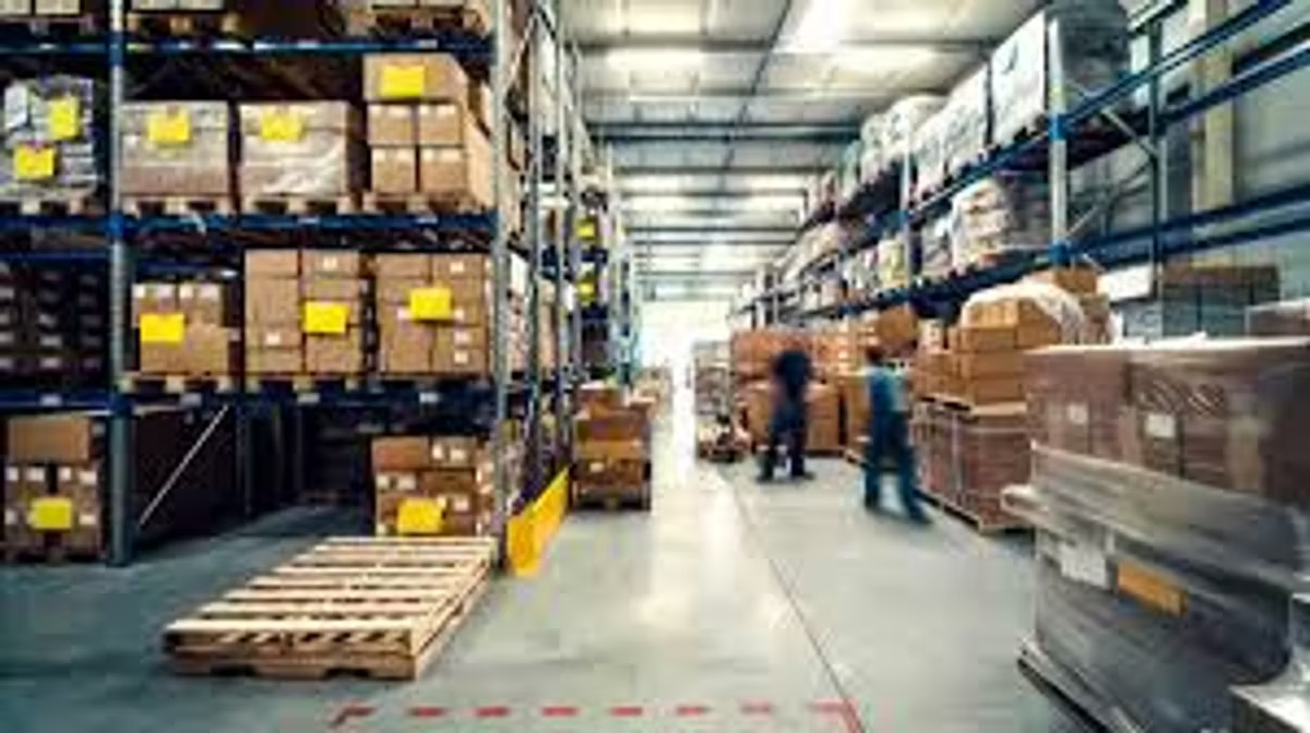 A warehouse aisle lined with tall racking full of boxes and pallets, with workers moving stock in the blurred background.