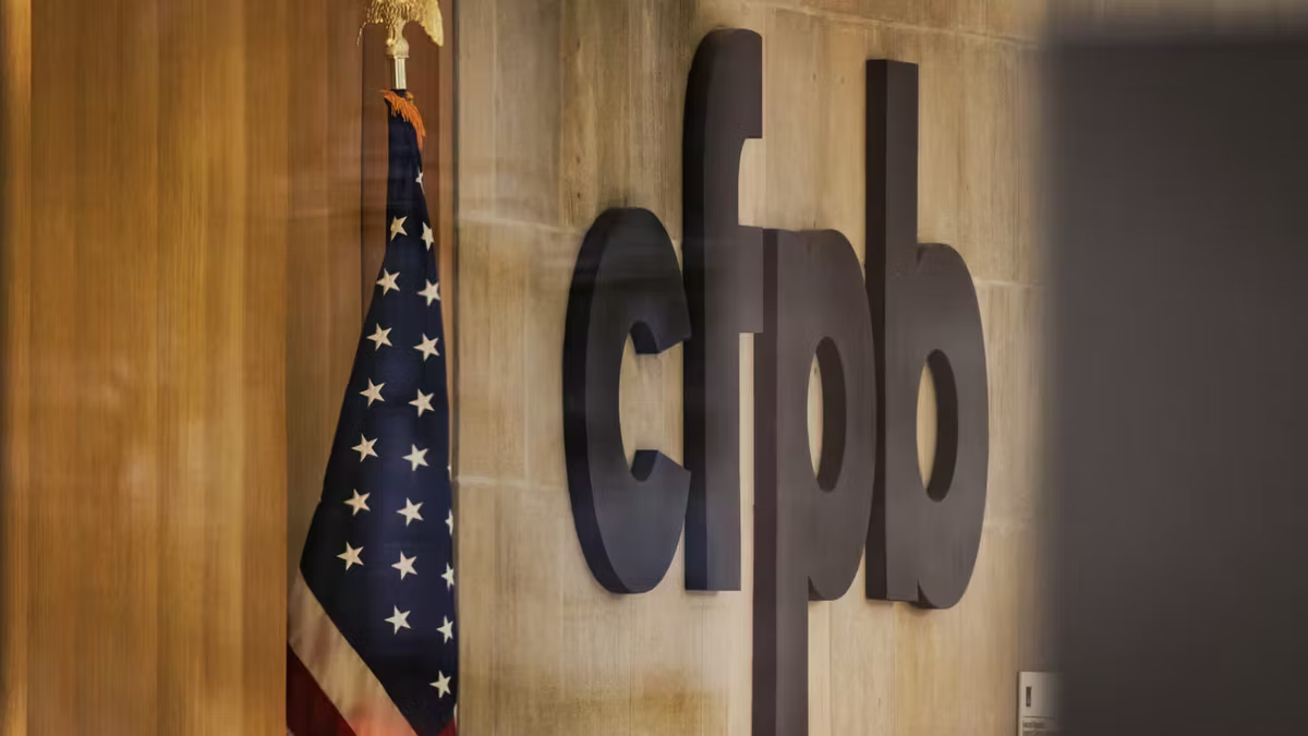 The cfpb logo mounted on a wood-panelled interior wall beside a United States flag, at the Consumer Financial Protection Bureau.