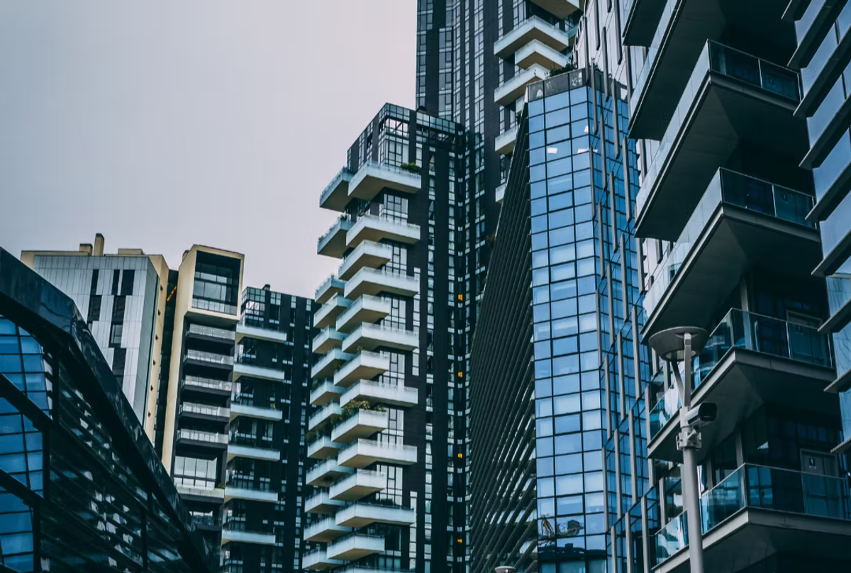 Modern high-rise apartment blocks in glass and concrete, seen from street level against an overcast sky.