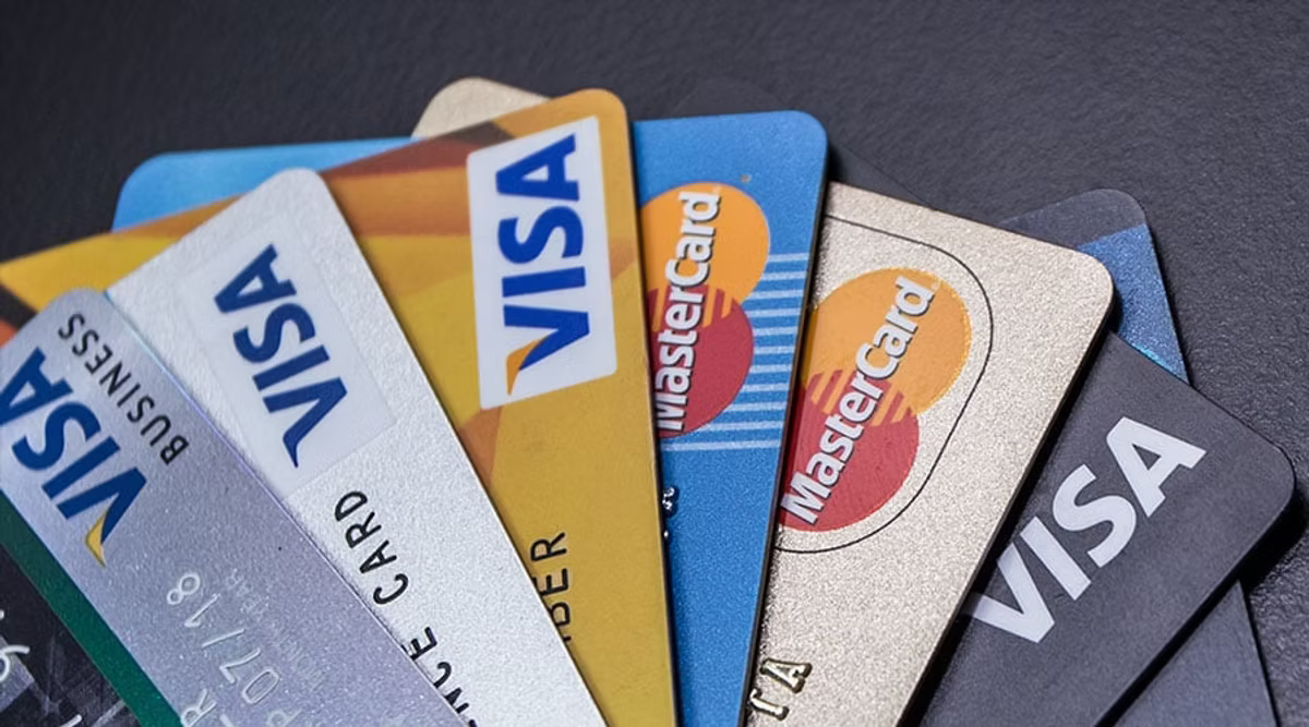 A fan of credit and debit cards spread across a dark surface, showing several Visa and Mastercard designs.