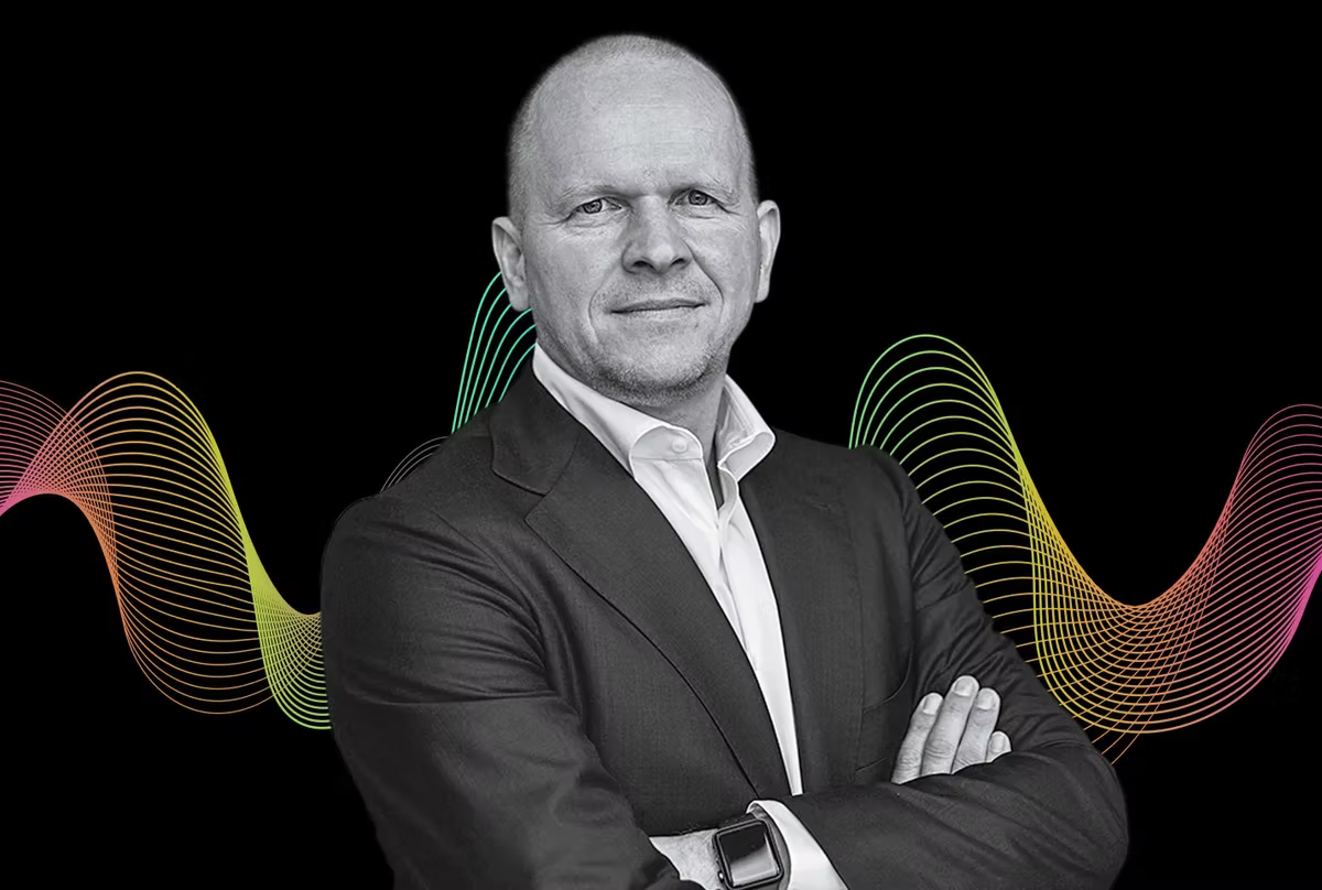 MasterCard CEO Michael Miebach in a suit with arms crossed, set against a black background with colorful wave patterns. Confident expression, wearing a smartwatch.
