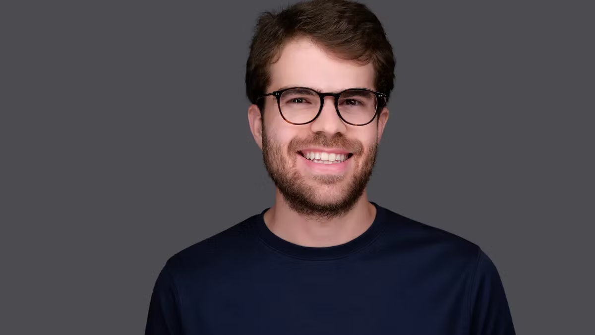 Brex CEO Pedro Franceschi with glasses and a beard in a dark shirt against a gray background. Mood is cheerful.