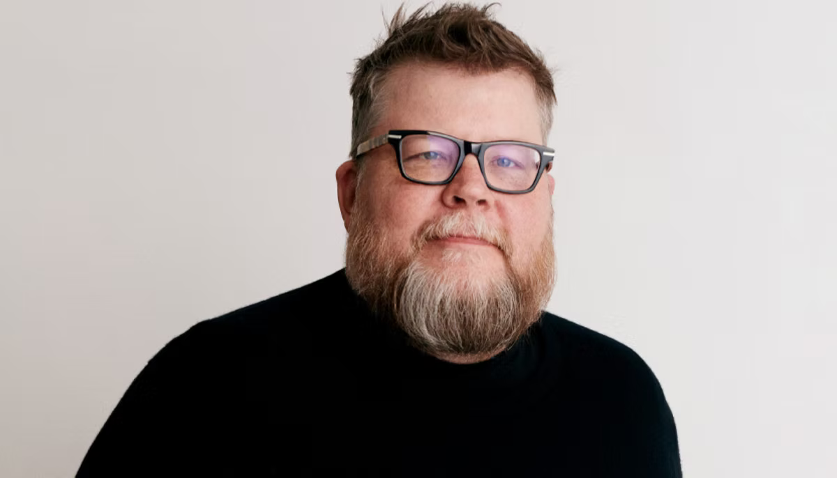 Etsy's Chief Product and Technology Officer Rafe Colburn a bearded man with glasses in a black shirt smiles slightly against a plain white background, exuding a calm and relaxed mood.