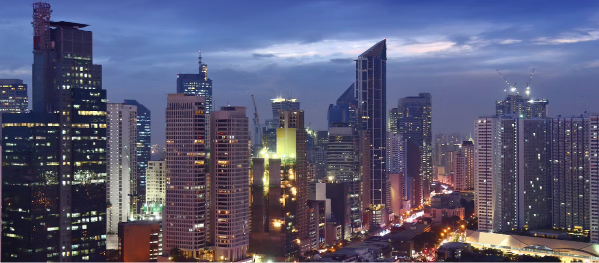 A city skyline of high-rise towers at dusk, lit windows and busy roads below a blue sky.