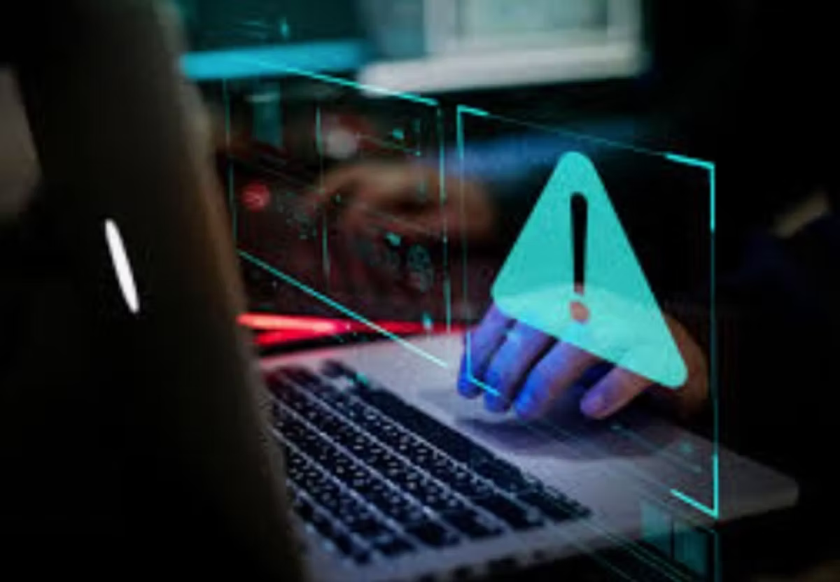 Someone typing at a laptop in a dark room, with a large glowing warning triangle projected above the keyboard.