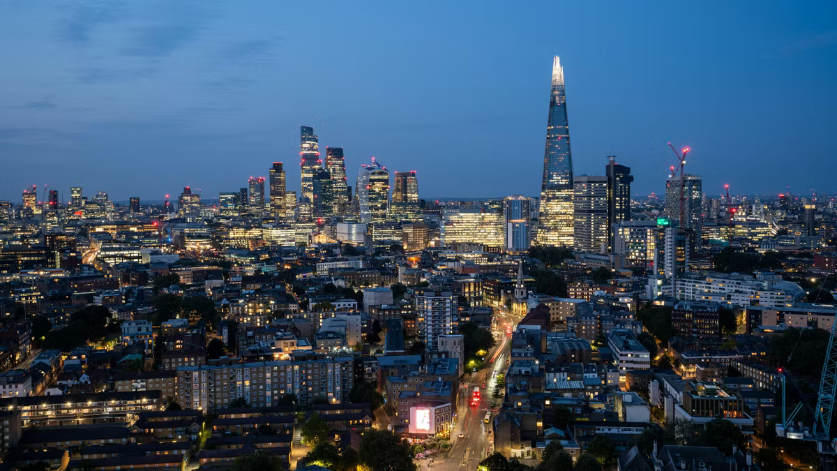 The London skyline at dusk, the Shard rising on the right and the City cluster on the left above lit streets.