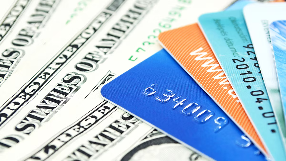 Several payment cards fanned out across US dollar banknotes, seen close up.