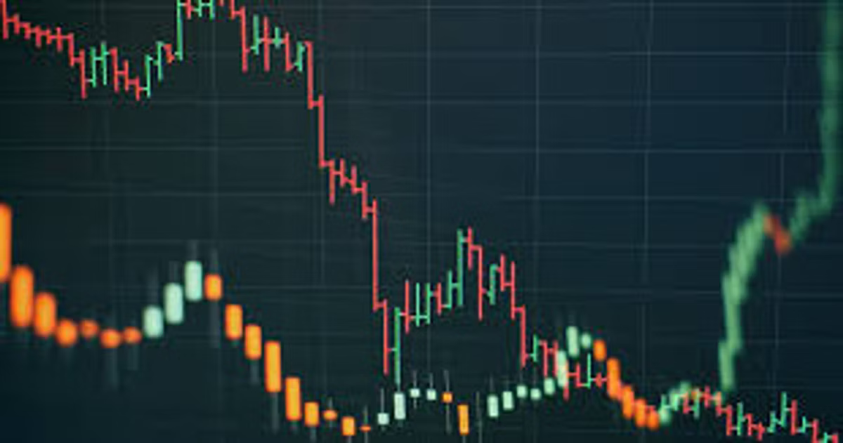 A close-up of a candlestick trading chart in red and green on a dark grid, the trend falling from left to right before a late green rally.