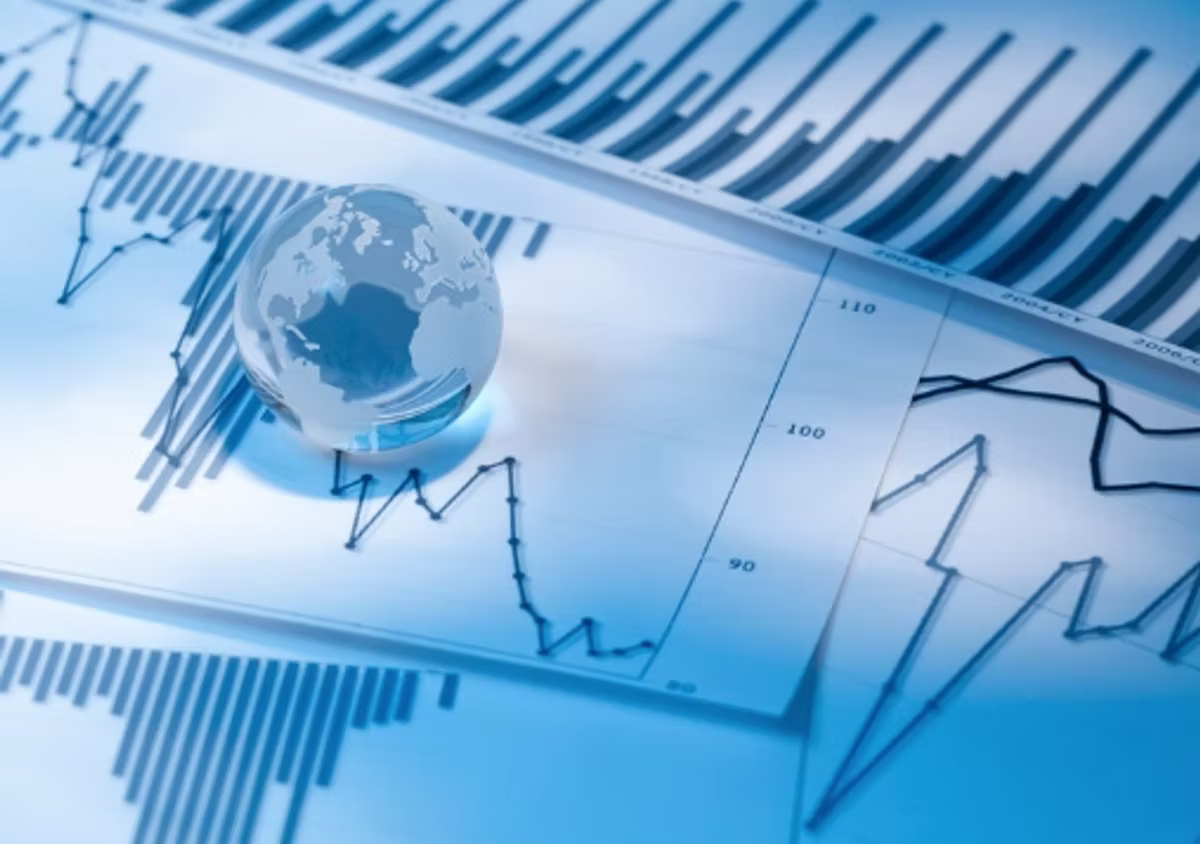 A glass globe resting on printed financial reports covered in bar and line charts, lit in blue.
