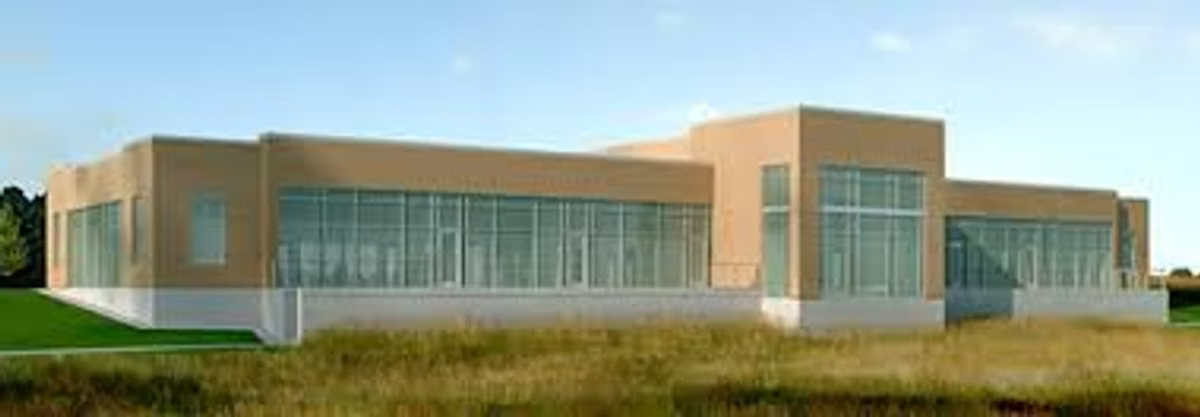 A low, modern single-storey office building in brick and glass, photographed from the grass verge under a clear sky.