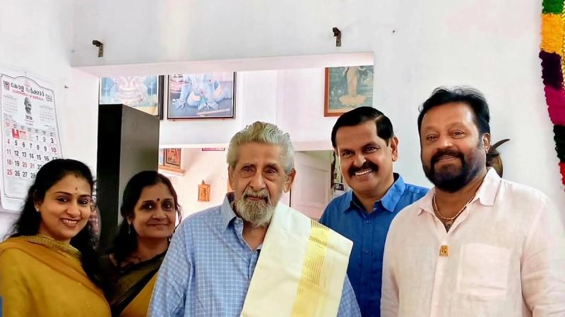 Veteran actor Madhu, in a blue shirt and gold-bordered shawl, stands at home with Suresh Gopi and family members