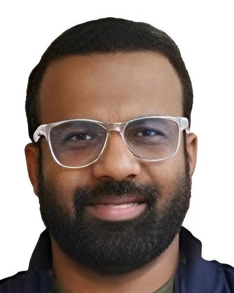 Jakes Bejoy in clear-framed glasses with a beard, close-up portrait