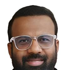 Jakes Bejoy in clear-framed glasses with a beard, close-up portrait