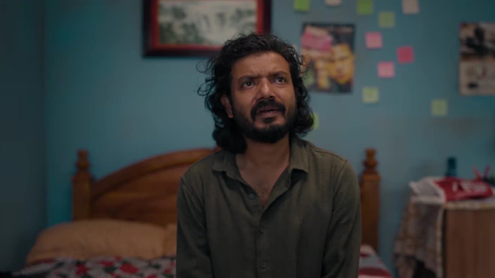 Sreenath Bhasi in an olive shirt sitting on a bed in a still from the Orijinal trailer