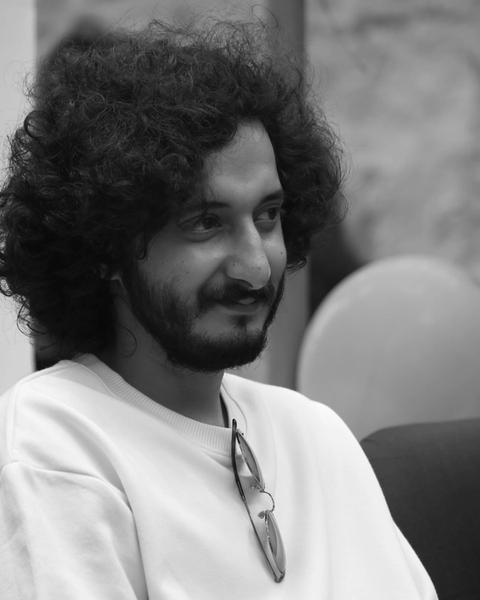 Sushin Shyam smiling in a white T-shirt, black-and-white photo