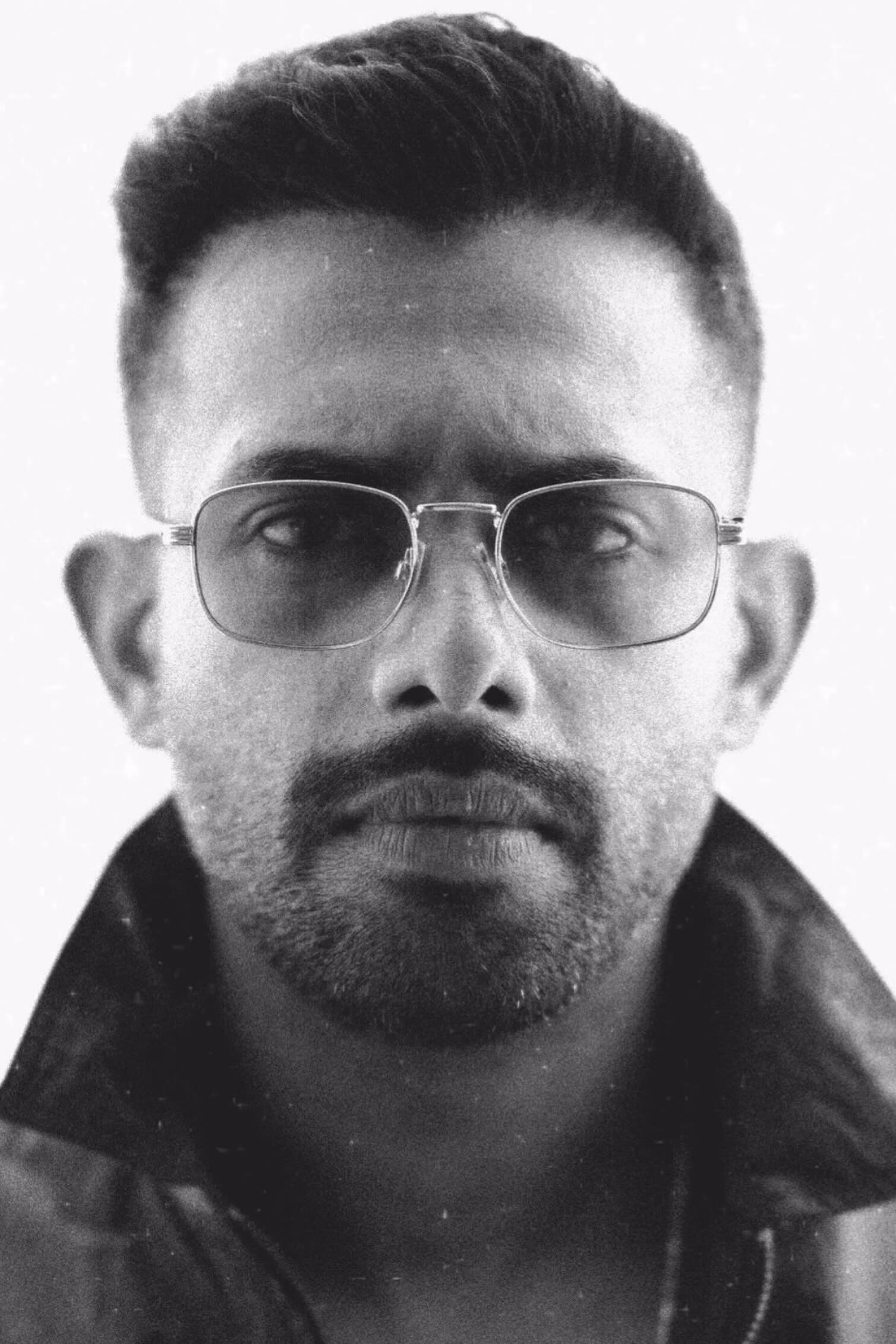 Arjun Ashokan in clear-framed glasses and a dark jacket, black-and-white portrait