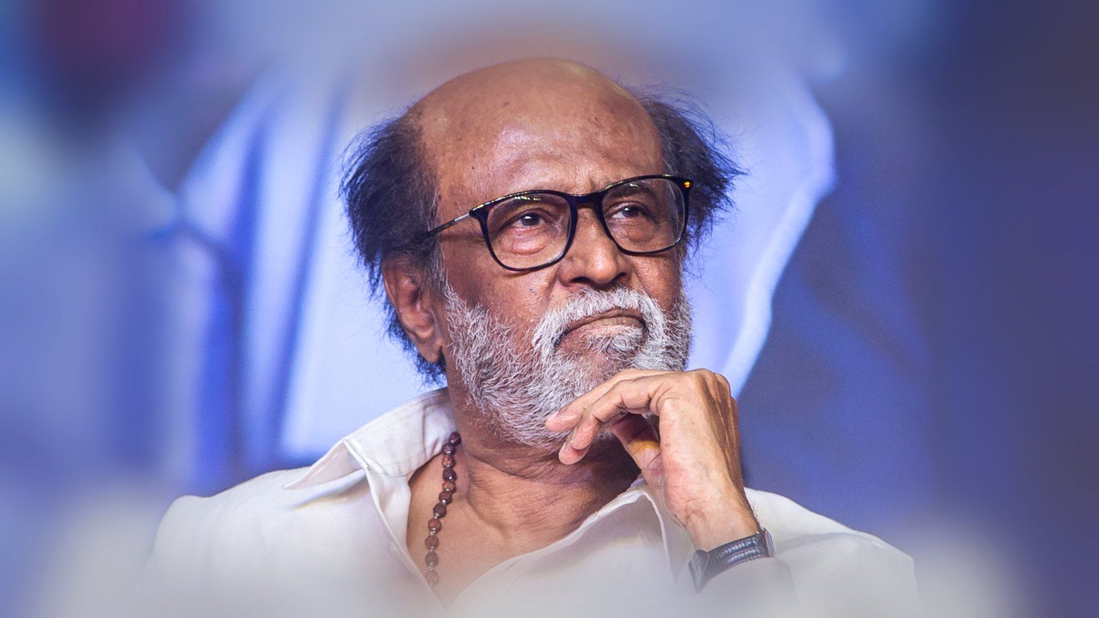 Rajinikanth in glasses, resting his chin on his hand at a public event